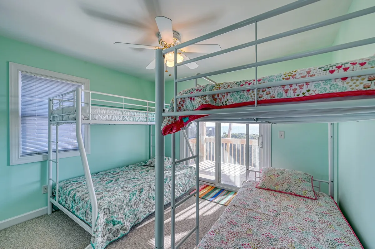 A playful interior scene featuring a spacious bunkroom with a bunk bed, single bed, and a door leading to a balcony. The bright, sunlit room is perfect for group sleepovers, late-night talks, and shared family experiences—especially for children.