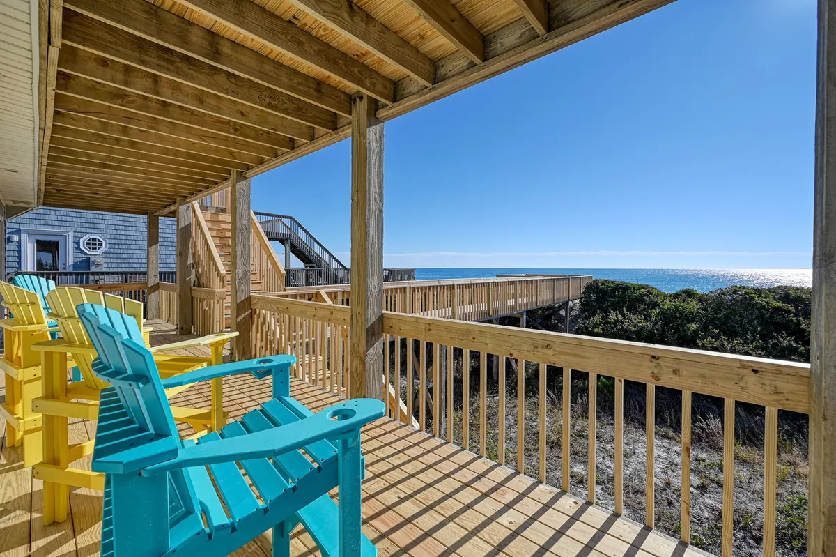 An exterior wooden deck outfitted with colorful Adirondack chairs, overlooking the ocean. The setting is tranquil, perfect for enjoying gentle ocean breezes, sipping coffee at sunrise, or unwinding as the sun sets.
