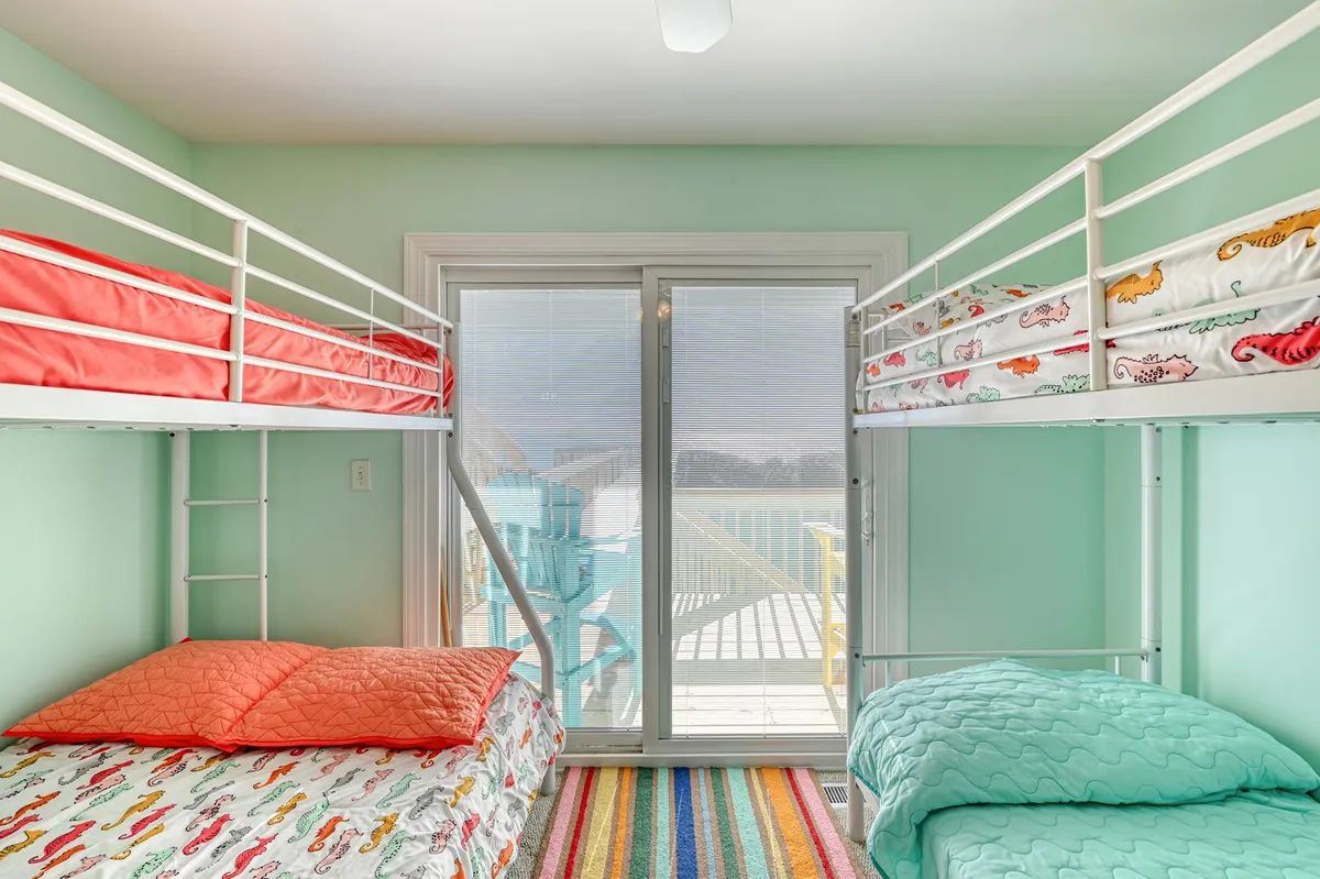 A second, equally inviting bunkroom, also featuring multiple bunk beds with vibrant bedding and a large sliding door letting in ample light. The playful atmosphere encourages activities such as playing games or reading, reinforcing the theme of a dedicated kid zone.