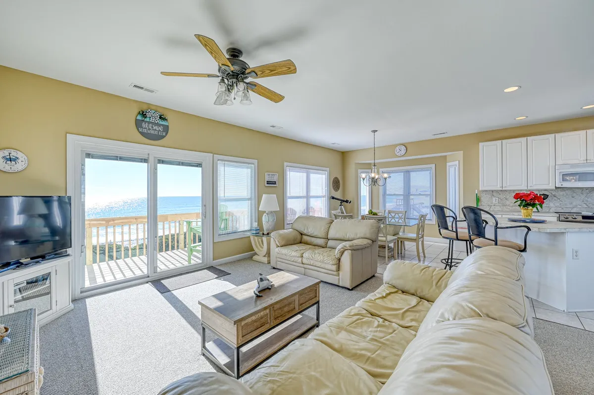 An airy, open-concept living space featuring a comfortable seating area, a dining table, and a modern kitchen. Large windows frame expansive ocean views, flooding the space with natural light and creating a seamless connection between inside and outside. The setting invites both relaxation and social gatherings.