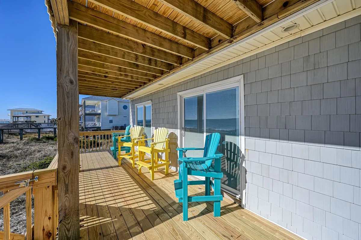 A cheerful, oceanfront deck with colorful chairs offers a stunning view of the shoreline. The deck is securely railed and overlooks the ocean, providing a relaxing spot to unwind with a pet while enjoying the salty breeze or sunrise.