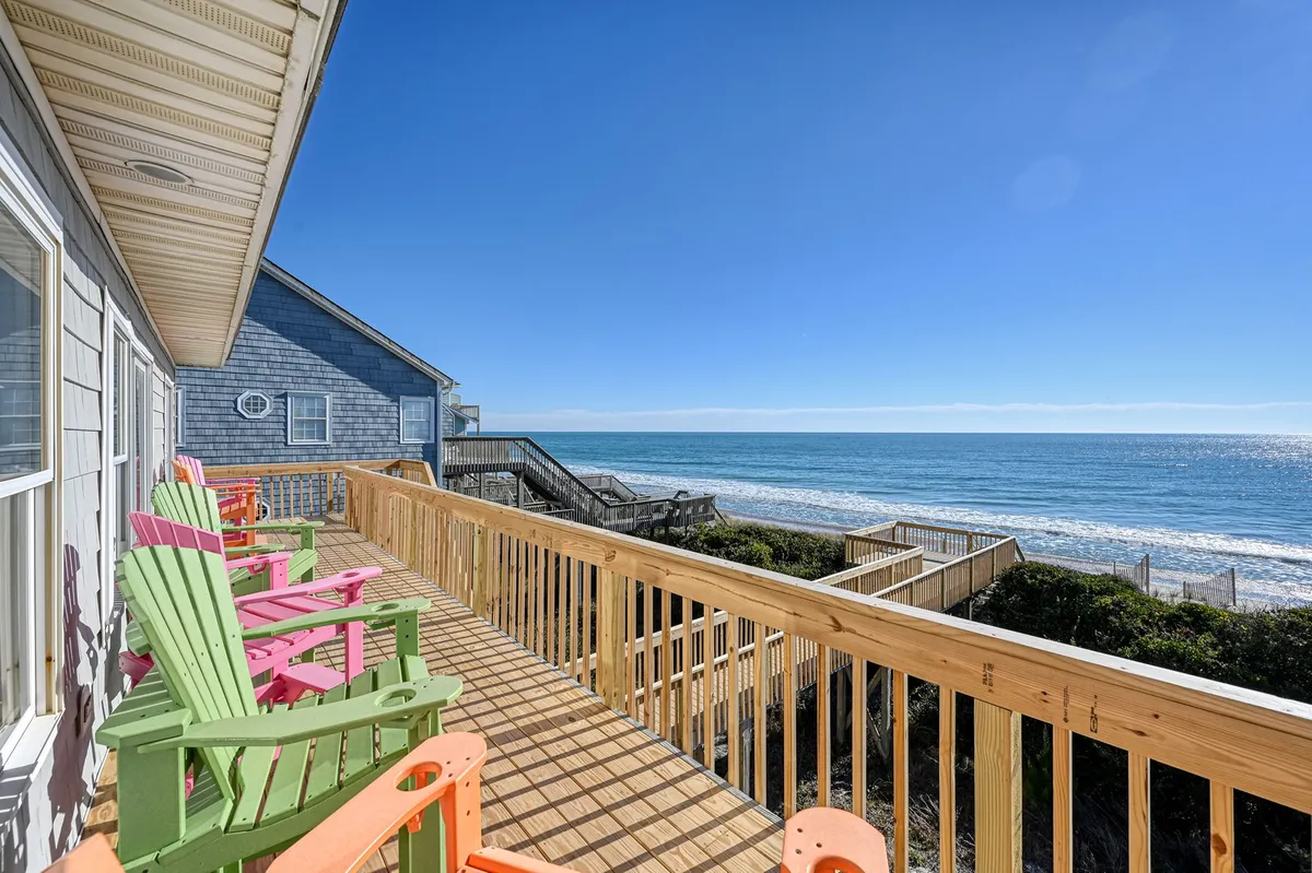 A cheerful exterior deck with colorful Adirondack chairs overlooking the beach and ocean waves. The space is perfect for relaxing, hosting gatherings, or simply enjoying morning coffee with a view.