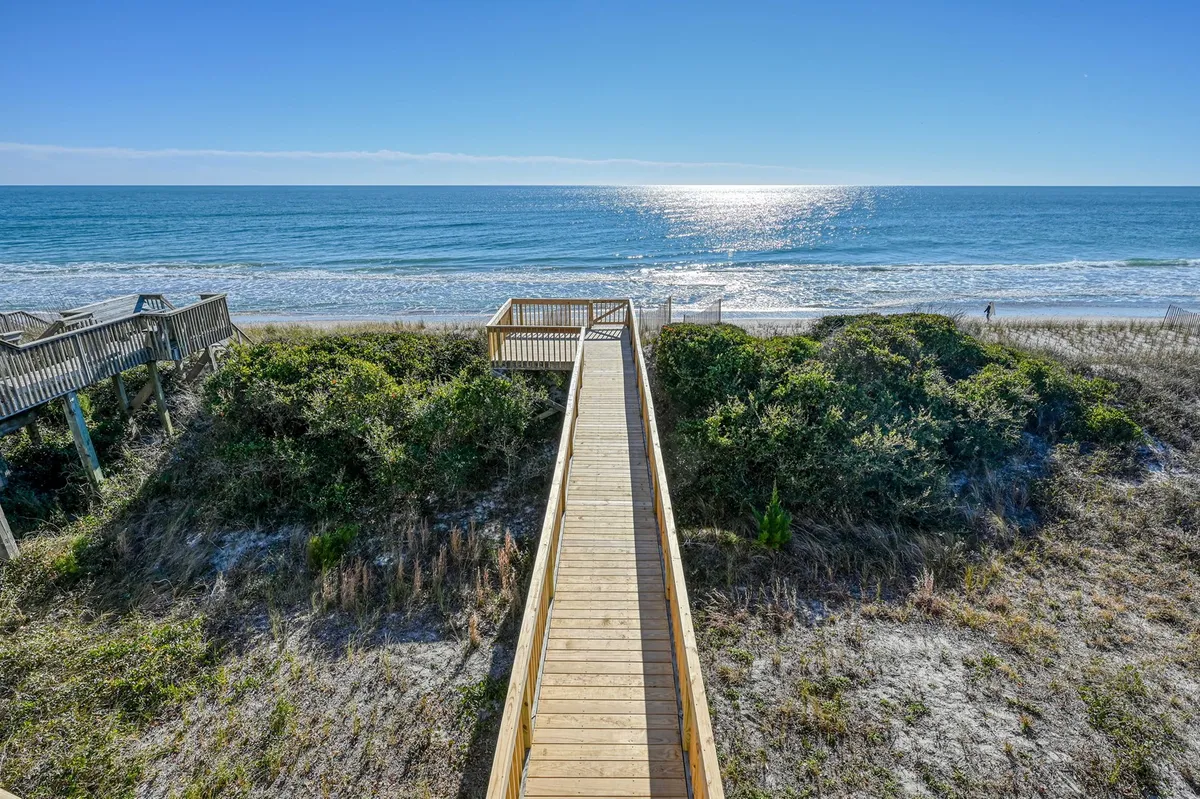 A wide wooden walkway stretches over sand dunes toward the open ocean, creating a scenic, coastal atmosphere. The view invites adventure and effortless access for beach walks with pets.