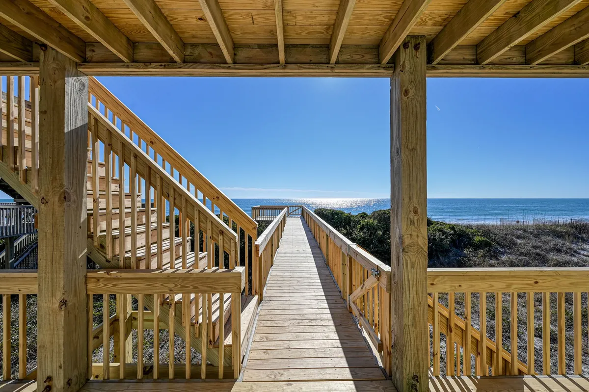 The image highlights a wooden staircase and a private boardwalk leading directly to the beach with the ocean in view. The path is flanked by natural dunes and beach grasses, emphasizing the easy transition from the home to the shoreline and the outdoor lifestyle promoted in the section.
