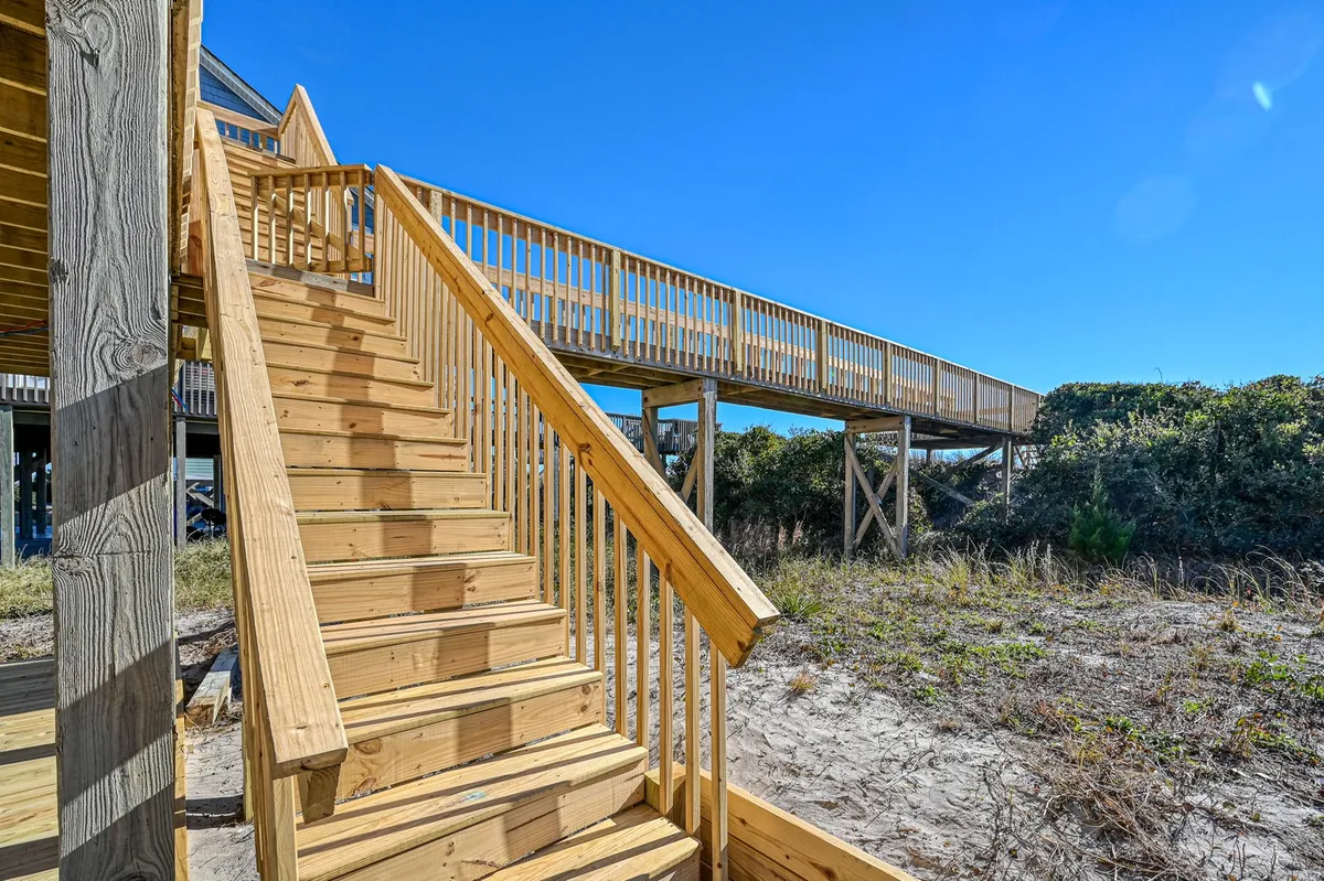 This exterior image features a wooden stairway and walkway surrounded by lush greenery, suggesting a peaceful, residential neighborhood perfect for strolls. The path leads toward the beach, evoking the idea of easy beach access for both pets and their owners.