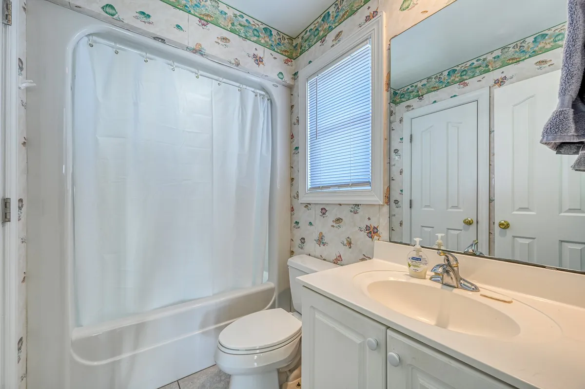 A modern, fresh hallway bath with a bathtub, sink, mirror, and toilet. The space is filled with natural light, and the layout is practical for families and kids coming back from the beach. The bath is tidy and inviting, ideal for quick clean-ups after active days.
