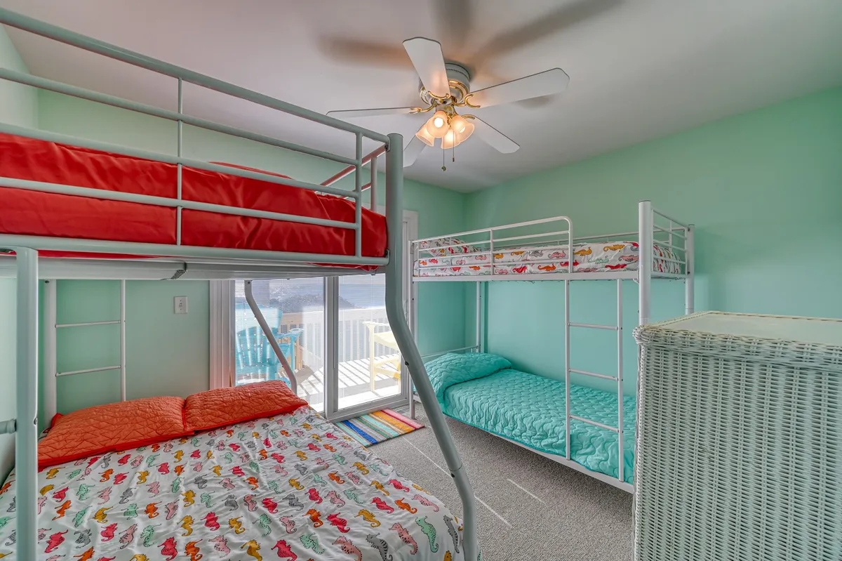 A bright and inviting bunkroom featuring twin-over-twin and twin-over-full bunk beds, all dressed in colorful bedding. Natural light pours in from a window, illuminating a cozy reading nook and creating a playful, comfortable atmosphere perfect for kids. The arrangement clearly shows multiple bunks, emphasizing the room's sleepover-friendly setup.