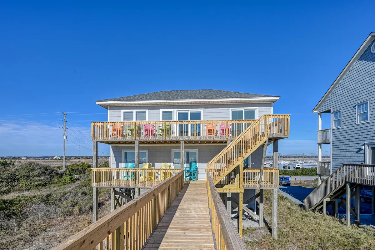 A cheerful exterior scene featuring a wooden deck adorned with colorful chairs, a wooden walkway, and the inviting structure of a modern beach house. The scene suggests relaxation, socializing, and seamless transitions between indoor and outdoor living.