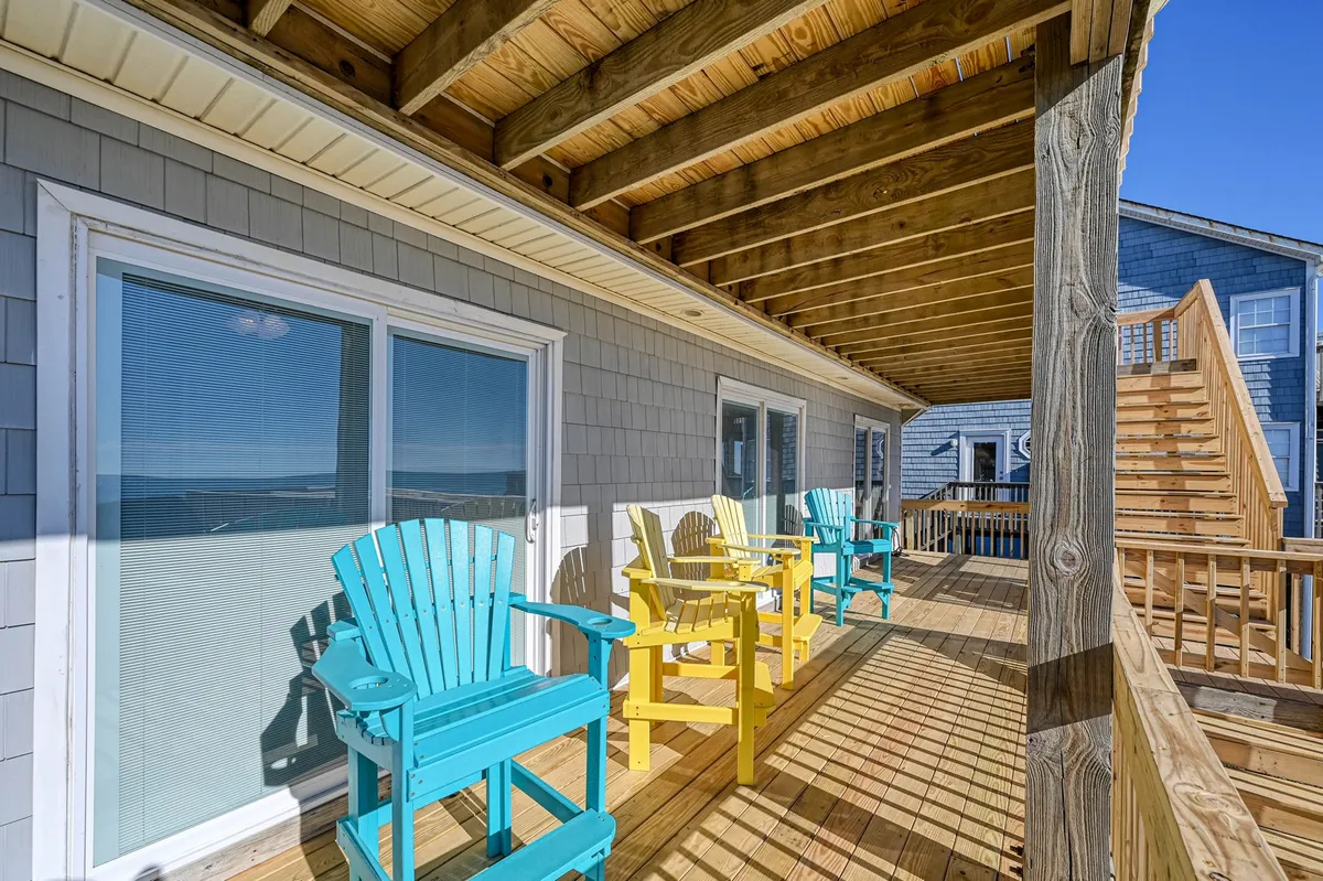 This image features an exterior wooden deck lined with vibrant Adirondack chairs and large windows reflecting daylight. The setup is perfect for socializing, watching sunrises, or enjoying evening conversations under the stars, with ample space to gather and take in the scenery.