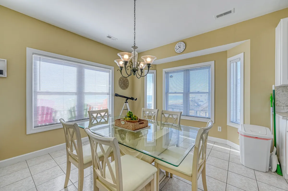 A warm, inviting dining area with a large table under a stylish chandelier, a telescope by the window, and expansive views through the windows. The space is designed for family meals, entertaining, and enjoying the ocean horizon.