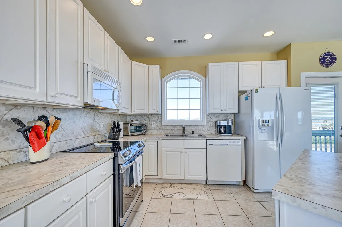 A modern kitchen with stainless steel appliances, granite countertops, and a large window letting in plenty of sunlight. The space is well-equipped for cooking and socializing, ideal for prepping meals as described in the section.